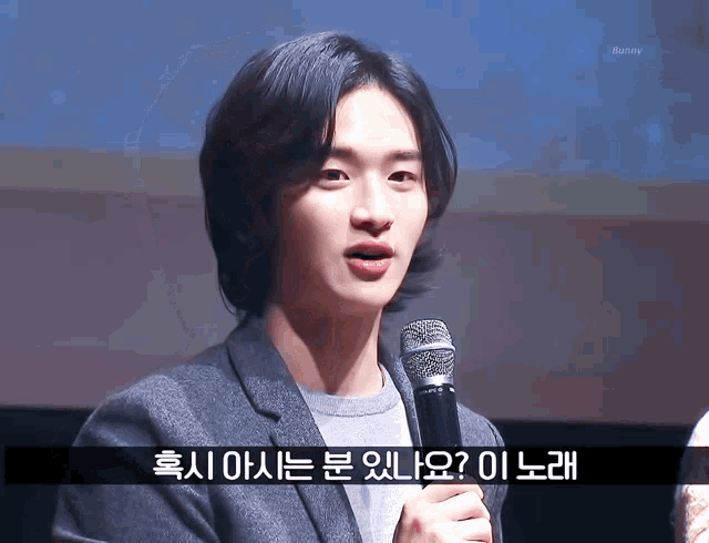 a man in a suit holds a microphone in front of a screen with bunny written on it