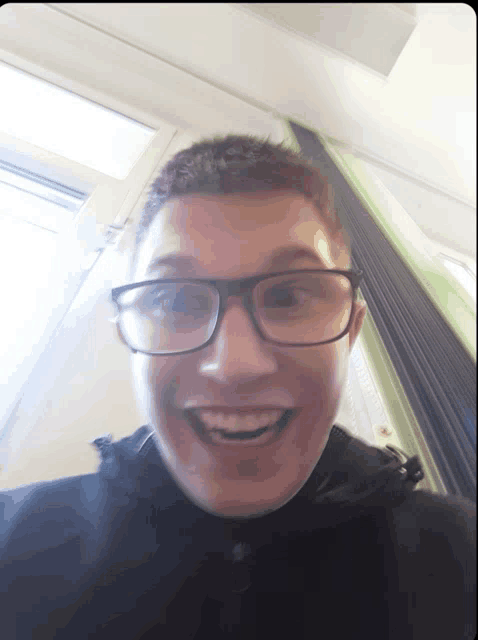 a young man wearing glasses and a black jacket is smiling