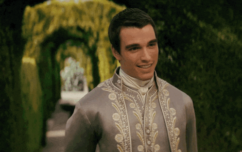 a man in a grey and gold embroidered jacket smiles for the camera