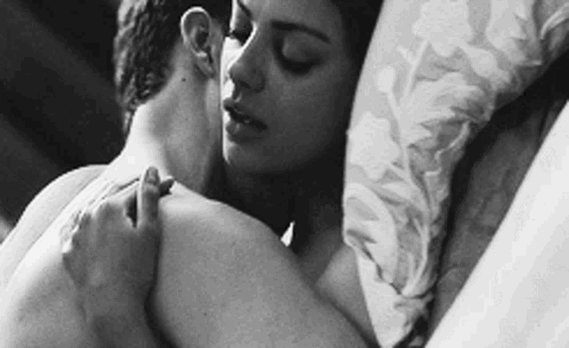 a black and white photo of a man and woman hugging in bed .