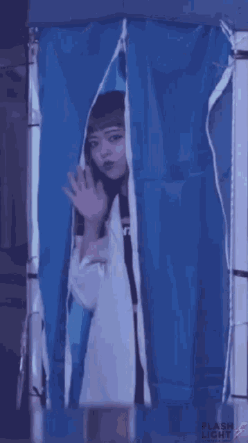 a woman stands behind a blue curtain that says flash light on it
