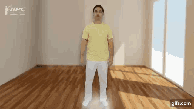 a man in a yellow shirt and white pants is standing in an empty room with a wooden floor .