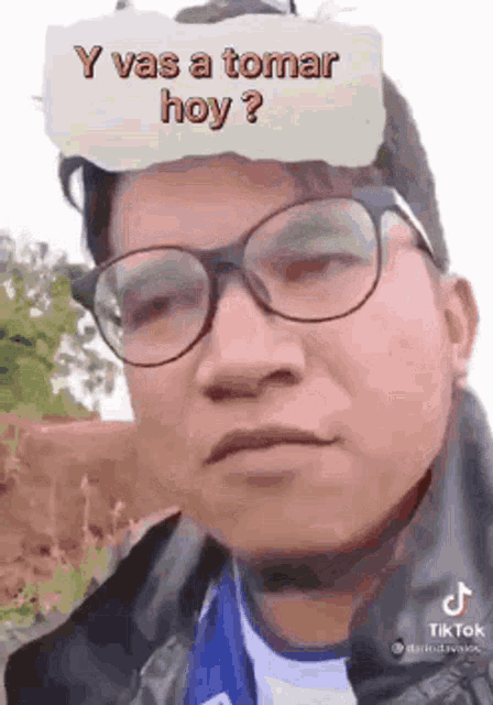 a man with glasses is wearing a paper on his head that says y vas a tomar hoy ?