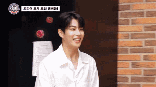 a man in a white shirt is smiling in front of a brick wall and a sign that says ' a ' on it