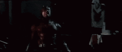 a man in a red superhero costume is holding a gun in a dark room .