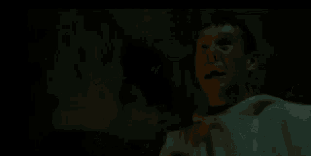 a man in a white shirt is standing next to a black animal in the dark .