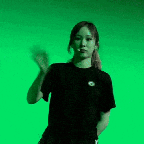 a woman in a black t-shirt is standing in front of a green screen .