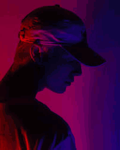a man in a baseball cap is standing in front of a purple and red background .