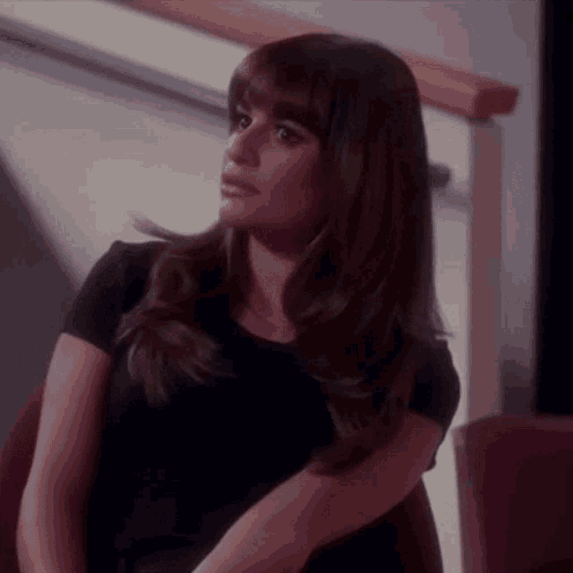 a woman in a black shirt is sitting in a chair and looking away from the camera .