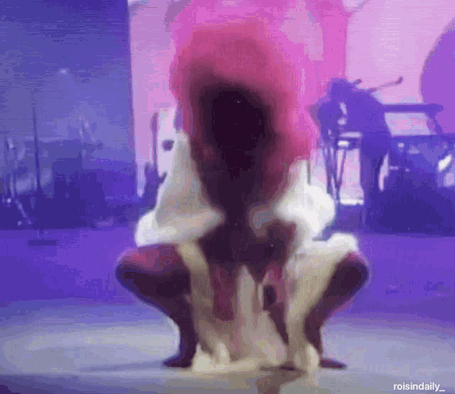 a person with pink hair is squatting on a stage