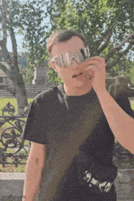 a man wearing sunglasses and a black shirt is talking on a cell phone .