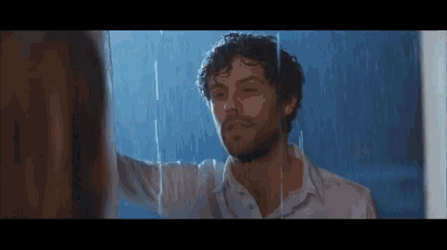 a man in a white shirt is standing in the rain looking at a woman .