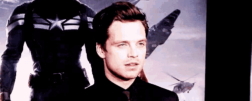 a man in a black suit is standing in front of a poster of captain america .