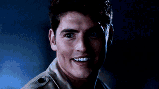 a young man in a tan jacket is smiling in the dark .