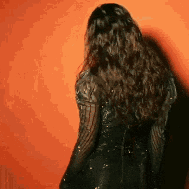a woman in a black dress is standing in front of a red wall