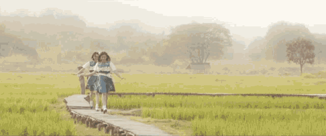 two young girls are running in a field holding hands and smiling .