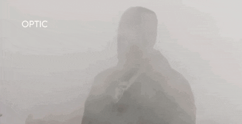 a man wearing a necklace and a hat is standing in a foggy room .