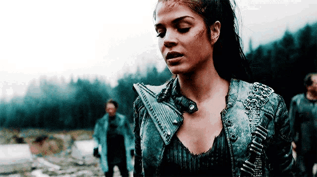 a woman wearing a leather jacket and a necklace is standing in a field