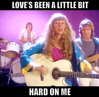 a woman is playing an acoustic guitar in front of a band with the words love 's been a little bit hard on me