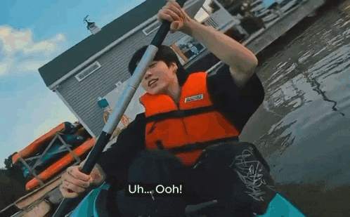 a young man in a life jacket is rowing a kayak on a lake .