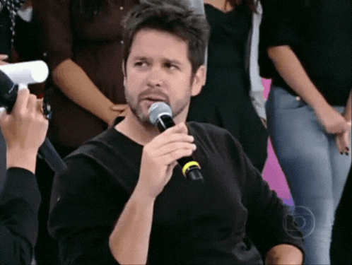a man in a black shirt is holding a microphone and talking into it