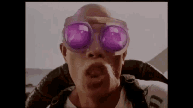 a man wearing a pair of purple sunglasses is blowing a kiss .
