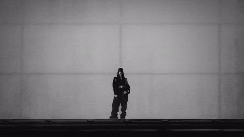 a black and white photo of a woman standing in front of a white wall .