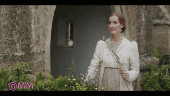 a woman in a white coat is standing in front of a building holding flowers