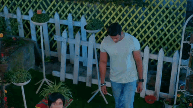 a man standing in front of a white picket fence with potted plants