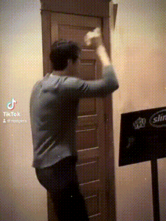 a man is standing in front of a wooden door with a sign that says tiktok on it .