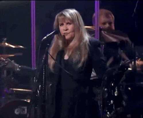 a woman singing into a microphone in front of a drum set that says dw on it