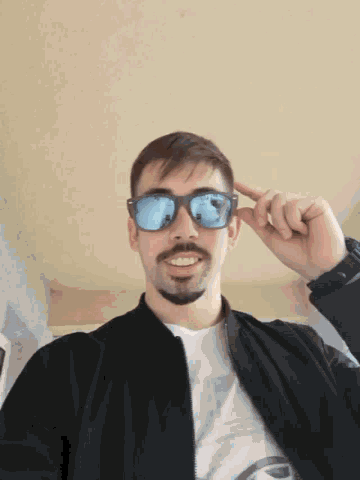a man with a beard is holding a pair of sunglasses in front of his face .