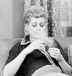a woman is smoking a cigarette while sitting on a couch in a black and white photo .