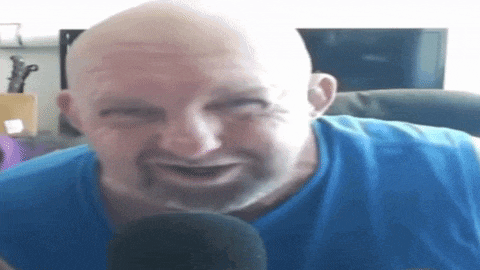 a bald man with a beard is wearing a blue tank top and talking into a microphone .