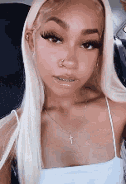 a woman with blonde hair and braces is wearing a white tank top and a necklace .