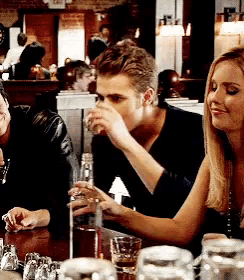 a man is drinking from a glass while sitting at a table with other people