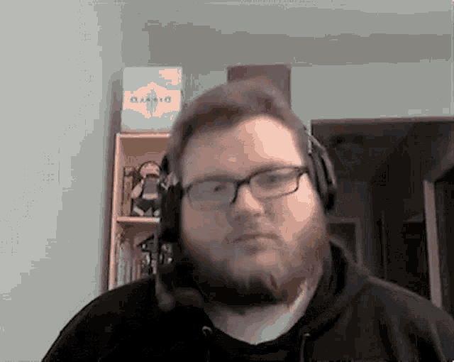 a man with a beard and glasses is wearing headphones and making a funny face .
