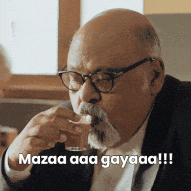 a man with glasses and a beard drinking from a glass with the caption mazaa aaa gayaaa !!