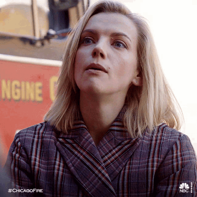 a woman in a plaid jacket stands in front of a sign that says engine c.