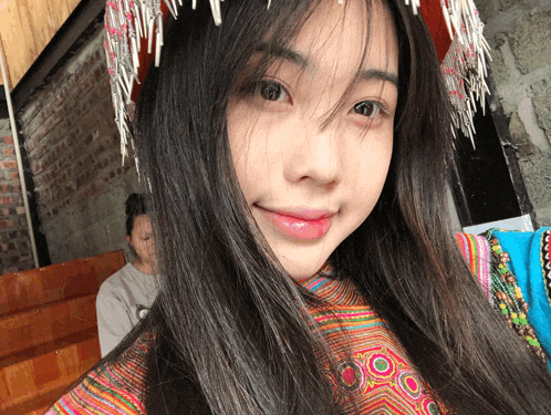 a woman wearing a colorful dress and a headdress looks at the camera with a smile on her face