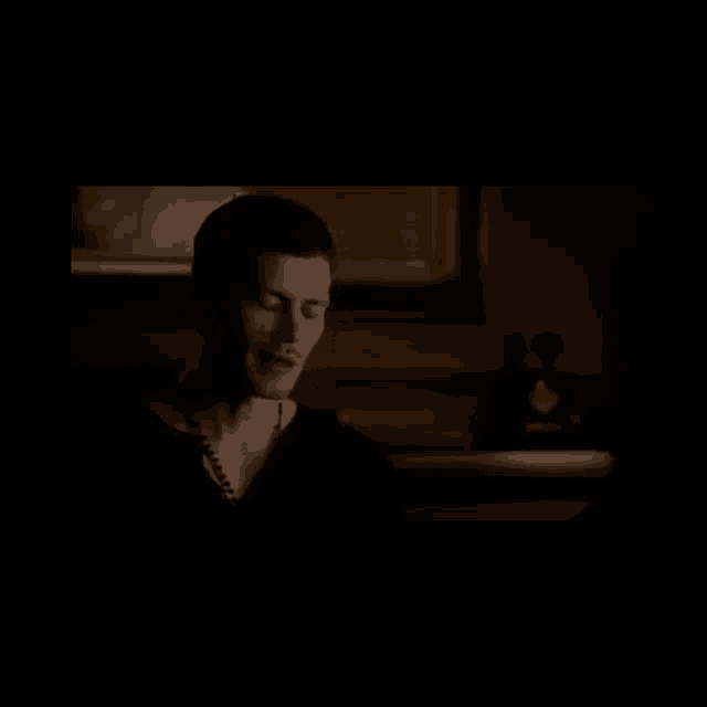 a man is sitting in a dark room with a bottle of alcohol in the background .