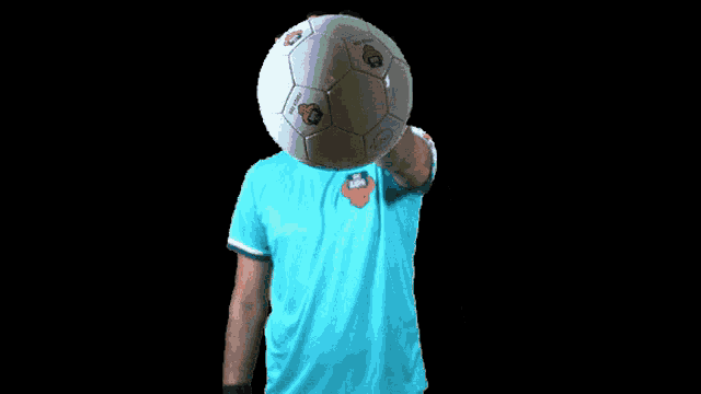 a man in a blue shirt holds a soccer ball over his head