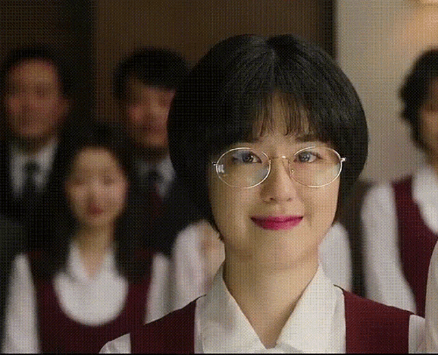 a woman wearing glasses is smiling in front of a crowd of people