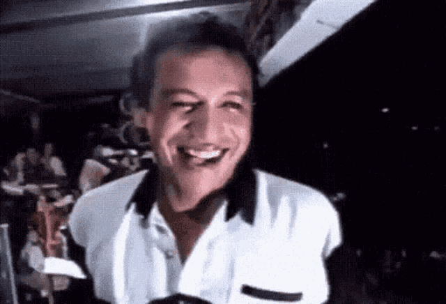 a man in a white shirt is smiling and laughing in a dark room .