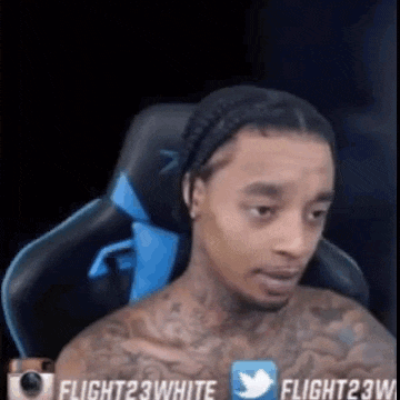 a shirtless man with tattoos is sitting in a gaming chair and looking at the camera .