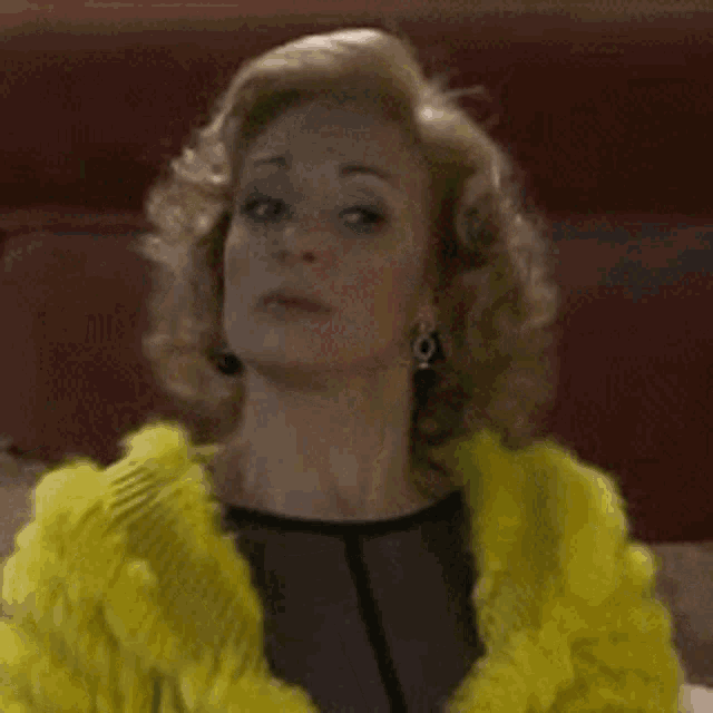 a woman with curly hair wearing a yellow fur coat and earrings