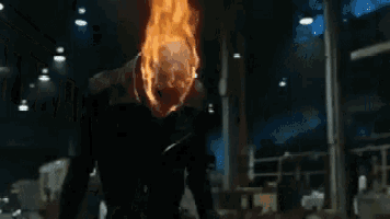a ghost rider is standing in a dark room with a fireball coming out of his head .