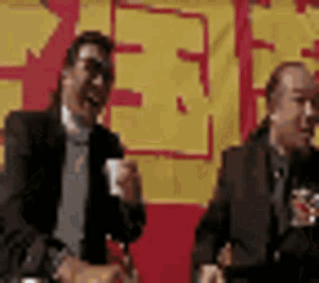 two men are standing next to each other in front of a yellow and red banner .