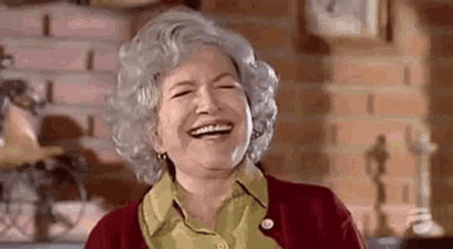 an elderly woman is laughing with her eyes closed in a room .