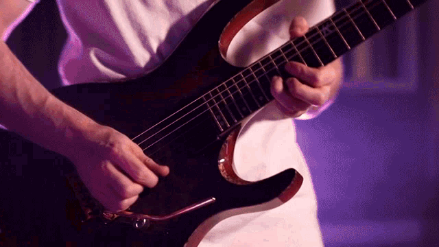 a man in a white shirt is playing a black electric guitar